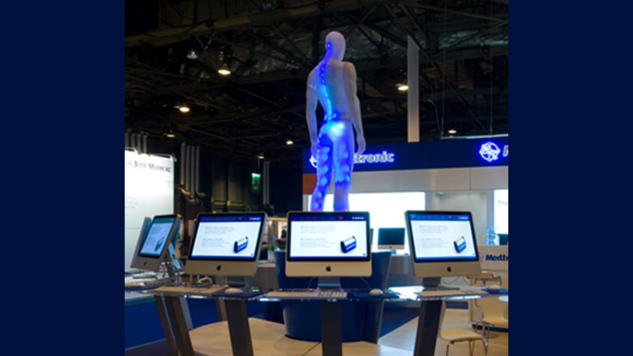 The Fliex attraction at a trade-show booth: a 3D figure above a row of touch screens