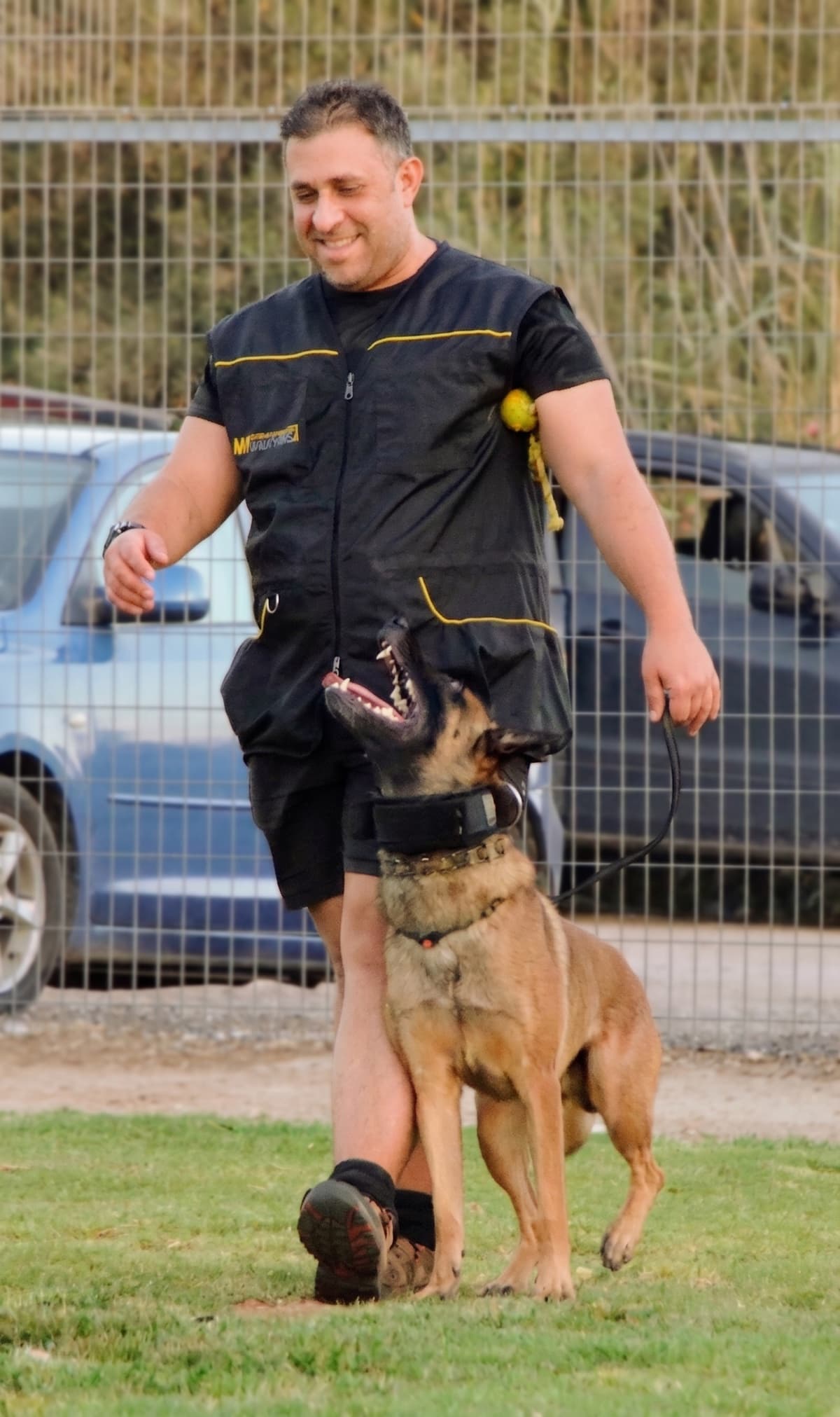 Almog smiling while training with Echo, his Belgian Malinois search-and-rescue dog, who looks up at him on the grass